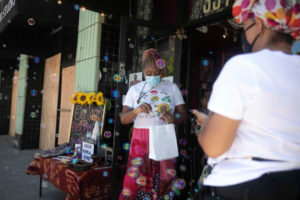 Lilliannia Ayers places a stick of sage in a bag while serving a customer at her store Queen Hippie Gypsy in downtown Oakland. All of the businesses on Ayers’ block were vandalized during recent protests earlier this week against the killing of George Floyd by police in Minneapolis. Photo by Anne Wernikoff for CalMatters